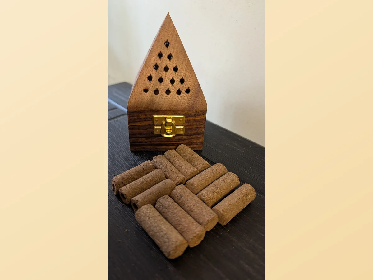 Wooden pyramid holder, latched shut, with a stack of cow dung dhoop sticks in front